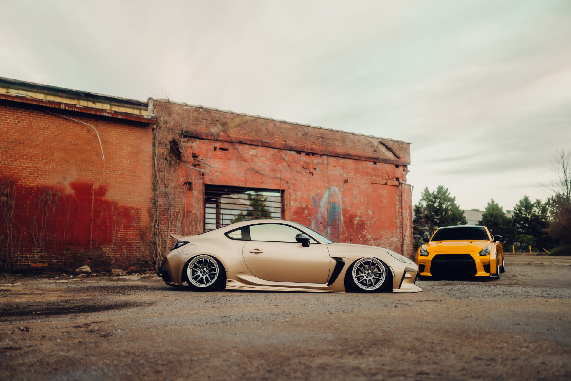 Toyota GR86 and Nissan R35 GT-R beside a weathered brick warehouse