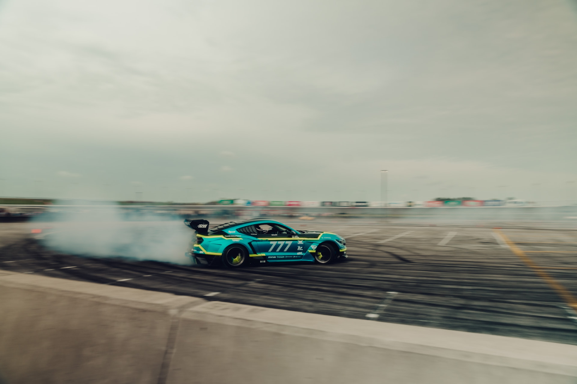Teal Ford Mustang drift car sliding through tire smoke on a track